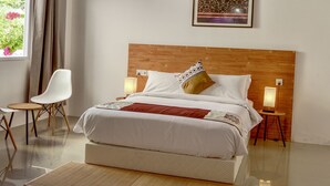 Une chambre avec un plafond en bois, un lit avec une literie blanche, une table de chevet avec une lampe, une chaise et une fenêtre avec des rideaux.