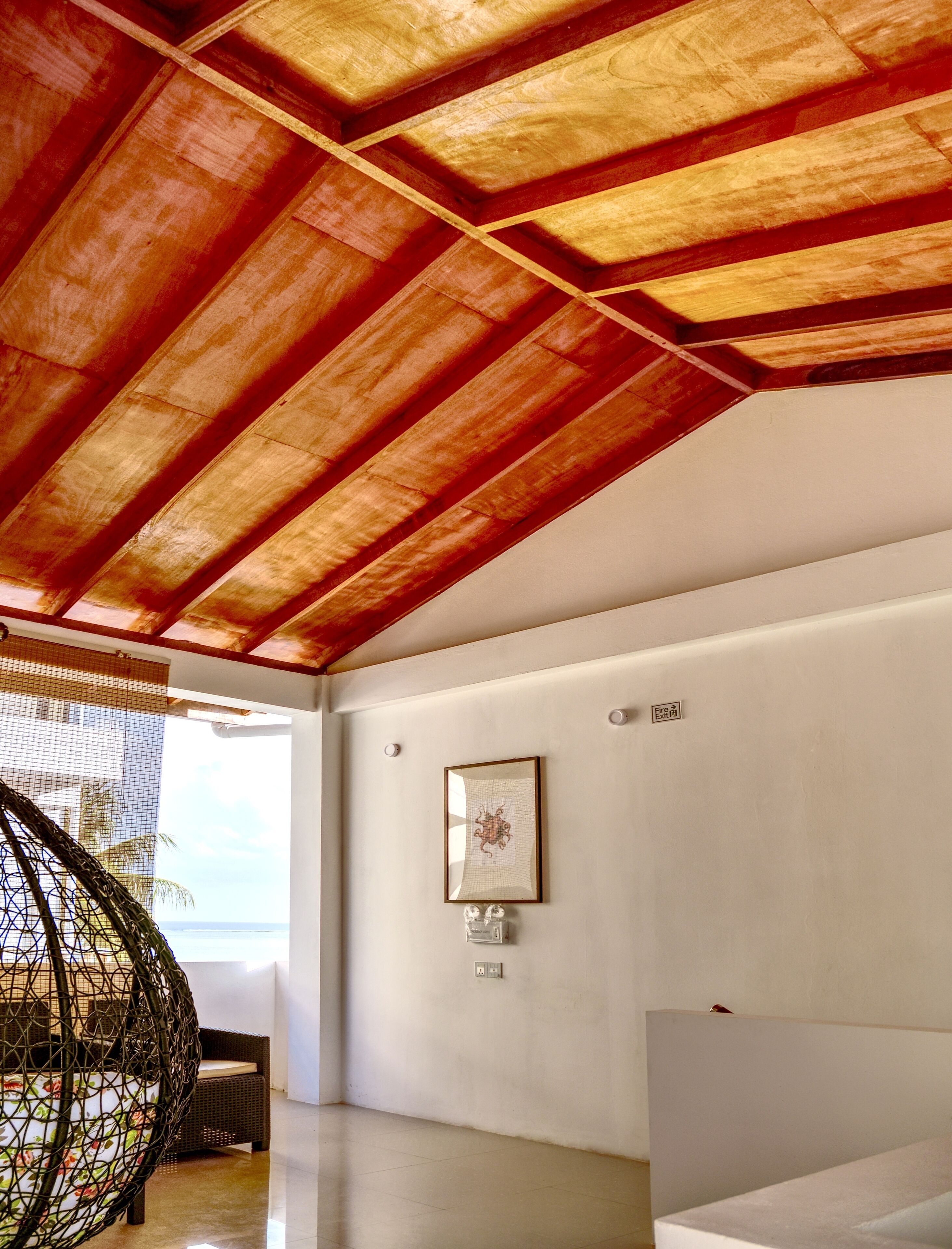A spacious room with a high ceiling, a framed artwork on the wall, and a fire exit sign.