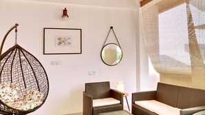 Une pièce avec un fauteuil suspendu, un tableau encadré, un miroir et deux canapés en osier.