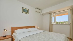 Slaapkamer met een bed, nachtkastjes, een airconditioner, een raam met uitzicht en een ingelijst schilderij aan de muur.