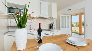 Een moderne keuken met witte kasten, een houten aanrecht, een vaas met bloemen, een wijnfles en een koffiezetapparaat.
