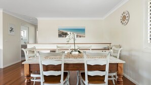 Un comedor con una mesa de mármol, sillas blancas y un cuadro de playa en la pared.