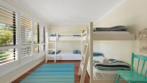Habitación con literas y vista a través de las persianas, una alfombra azul a rayas y una silla verde azulada.