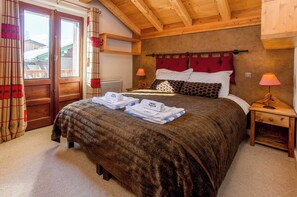 A bedroom with a large bed, two bedside tables, a wooden ceiling, and a view of the outside. - Chalet le Tremplin, Hot tub - Chamonix All Year (Chamonix)