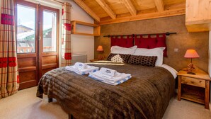 Ein gemütliches Schlafzimmer mit einem großen Bett, einem Holz-Kopfteil, zwei Nachttischen mit Lampen und Blick nach draußen durch eine Tür.