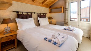 Ein Hotelzimmer mit zwei Betten, Holz-Kopfteilen, einem Nachttisch mit Lampe und einem Fenster mit Blick auf ein Holzhaus.