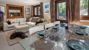 Ein Essbereich mit einem Glastisch, gedeckt für sechs Personen, umgeben von einem weißen Sofa und einem Hund, der auf einem Teppich liegt.