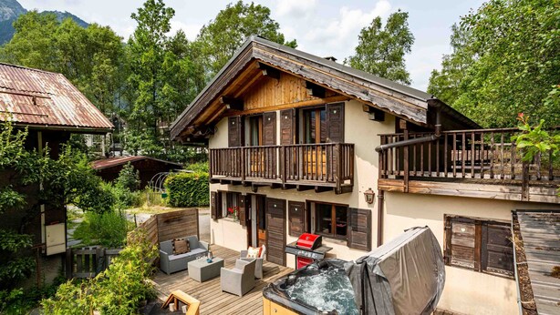 Eine Chalet mit einer Holzterrasse, Sitzgelegenheiten im Freien und einem Whirlpool.
