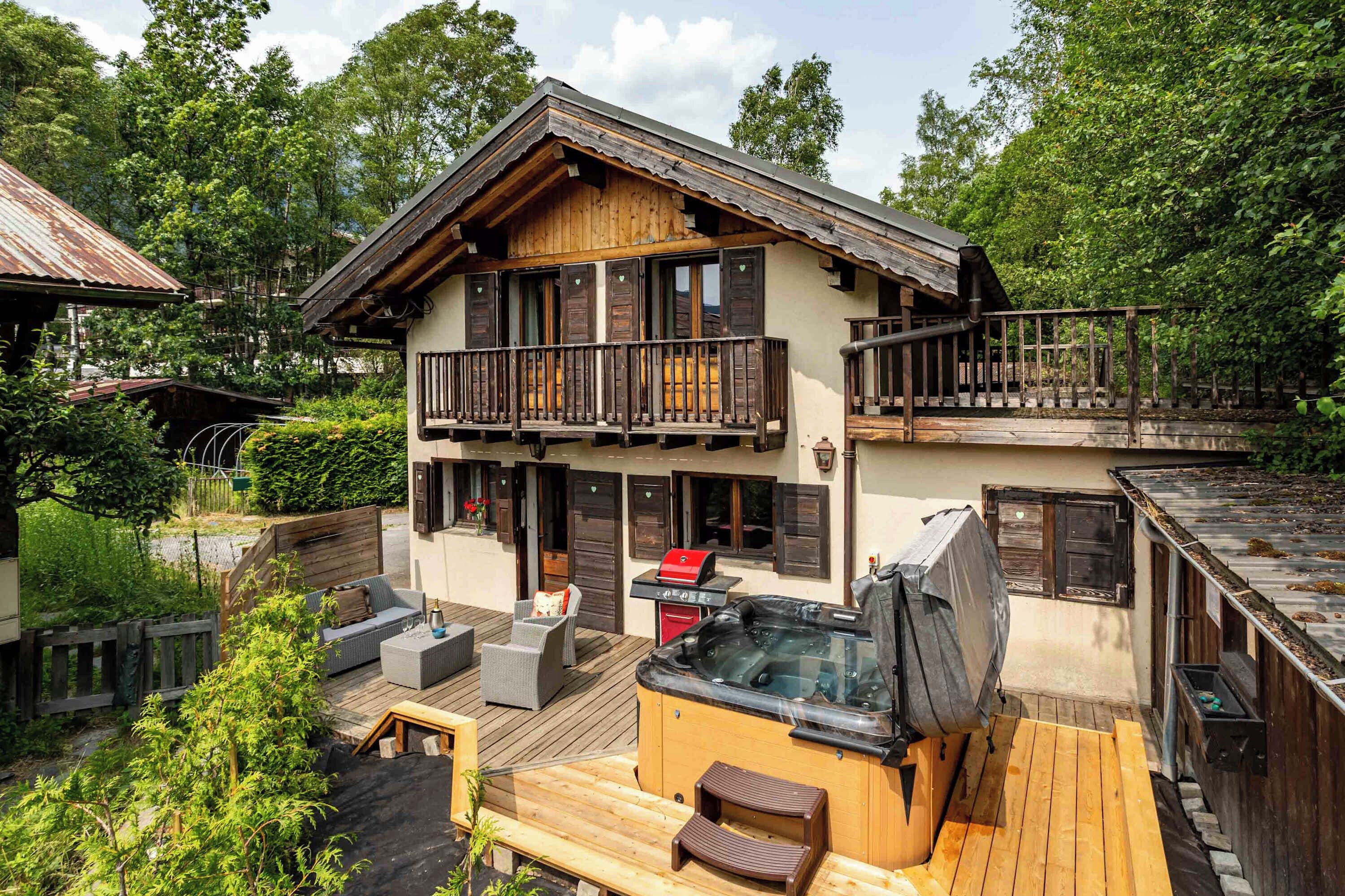 Een houten huis met twee verdiepingen, een balkon, een jacuzzi en buitenmeubels.