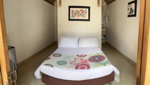 Une pièce étroite avec un lit, un tableau abstrait encadré accroché au mur, et une salle de bain visible au fond.
