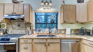A kitchen with wooden cabinets, a stainless steel stove, a dishwasher, and a window with a view of trees. - Modern Tollgate Home - HOT TUB, Half Acre Lot (Sisters)