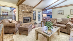 A spacious living room with a stone fireplace, leather sofas, and wooden beams on the ceiling. - Modern Tollgate Home - HOT TUB, Half Acre Lot (Sisters)