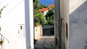 A narrow street with white buildings, a stone wall, and a view of the sea in the distance.
