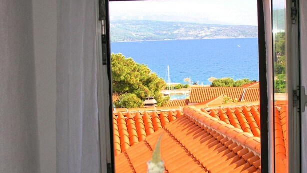A view from a balcony with terracotta tiles, overlooking a body of water and a distant coastline.