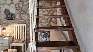 A wooden staircase with a rope handrail, leading to a room with a stone wall and a white chair.
