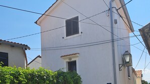 A two-story building with a white facade, a small window with shutters, and a metal staircase leading to the entrance.