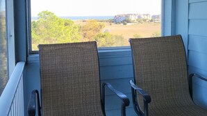 Two wicker chairs facing a window with a view of a beach and buildings. - RENOVATED LUXURY BEACH VILLA,Ocean view,3 bdrms each with smart tv and king bed (Hilton Head Island)