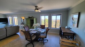 A dining area with a round glass table, four chairs, and a ceiling fan. There are large windows with a view of trees and a mountain. - RENOVATED LUXURY BEACH VILLA,Ocean view,3 bdrms each with smart tv and king bed (Hilton Head Island)