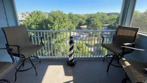 A balcony with two wicker chairs and a black and white striped lantern. The balcony overlooks a green landscape with trees and a road. - RENOVATED LUXURY BEACH VILLA,Ocean view,3 bdrms each with smart tv and king bed (Hilton Head Island)