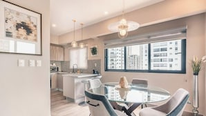 Une cuisine moderne avec une table à manger en verre, des luminaires suspendus et une vue sur la ville.