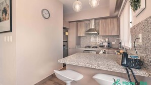 Une cuisine moderne dotée de plans de travail en granit, d’appareils électroménagers en acier inoxydable et de luminaires suspendus.