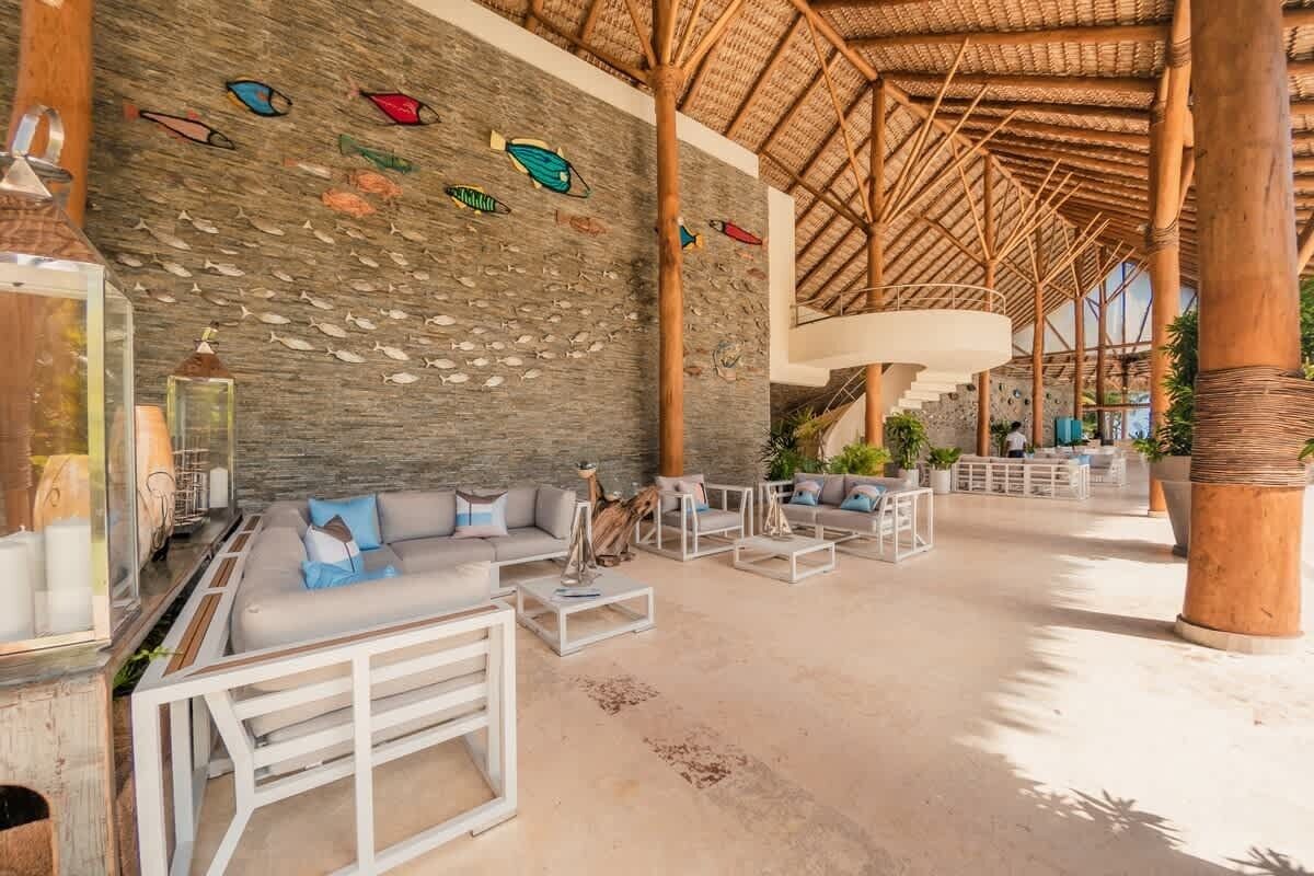 Un vestíbulo amplio con pared de piedra, techo de paja y una zona de estar con sofás y mesas.