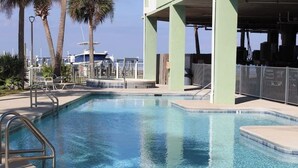 A clear swimming pool with a metal ladder, surrounded by a fence and palm trees.