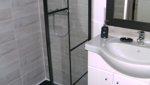 Un baño con cabina de ducha de vidrio, un lavabo blanco y un espejo.