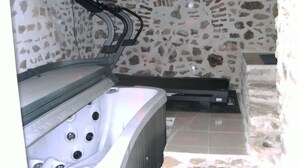 Un área de spa con pared de piedra, una bañera de hidromasaje y una camilla de masaje.