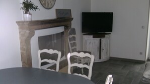 Un comedor con una mesa redonda, sillas blancas, chimenea, televisor y un aparador.