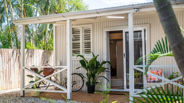 A covered patio area with a bicycle, a potted plant, and a wicker chair. - Oasis on the Esplanade (Manly)
