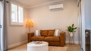 A living room with a brown leather sofa, a white ottoman, a floor lamp, and a potted plant. - Oasis on the Esplanade (Manly)