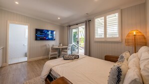 A hotel room with a bed, a TV mounted on the wall, a small table with chairs, and a window with blinds. - Oasis on the Esplanade (Manly)
