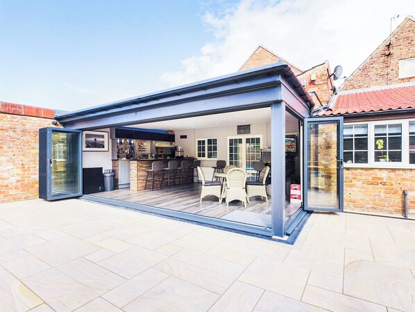 A modern kitchen with a bar area, a dining space with chairs, and a large sliding glass door leading to an outdoor patio.