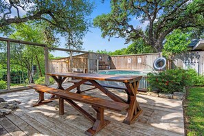Una terraza de madera con una mesa de picnic, un jacuzzi y un cerco de madera en un patio trasero.