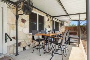 An outdoor patio with a stone wall, a covered dining area with a table and chairs, and a fan. - Cypress Star on the Medina | 4BR with Pool & River (Bandera)