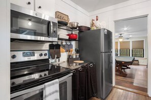 A kitchen with a microwave, stove, and refrigerator. There is a window with blinds and a ceiling fan.