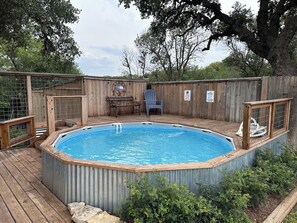 A hot tub with a wooden deck, surrounded by a wooden fence, and a patio area with a table and chairs. - Cypress Star on the Medina | 4BR with Pool & River (Bandera)