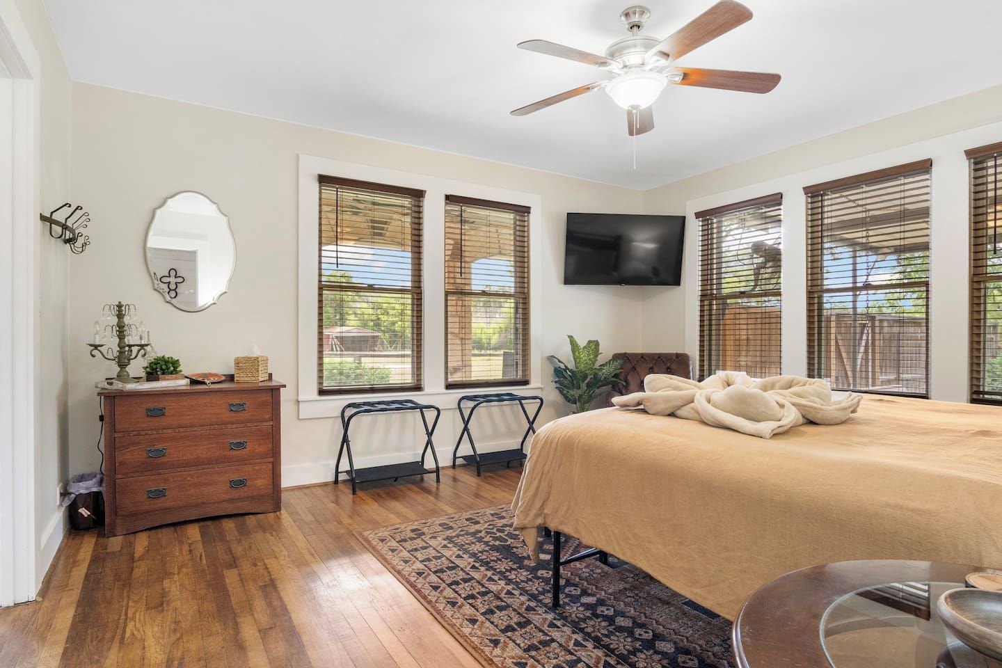 Quarto com cama, penteadeira, TV, ventilador de teto e janelas.