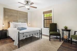 A bedroom with a bed, a chair, a table, a window, and a ceiling fan. - Cypress Star on the Medina | 4BR with Pool & River (Bandera)