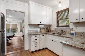 A kitchen with white cabinets, granite countertops, a stainless steel sink, and a window with blinds. - Cypress Star on the Medina | 4BR with Pool & River (Bandera)