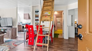 Eine moderne Küche mit Holzschränken, ein Essbereich mit roten Stühlen und eine Holzleiter zu einem Erkerraum.