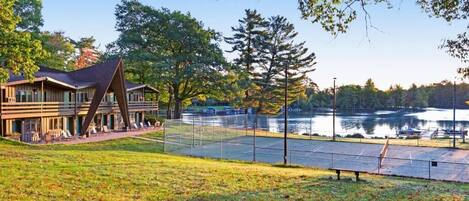 A lakeside hotel with a tennis court, outdoor seating, and a large building with a unique roof structure.