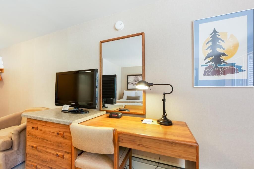 A hotel room with a wooden desk, a television, a mirror, a lamp, and a framed picture on the wall.