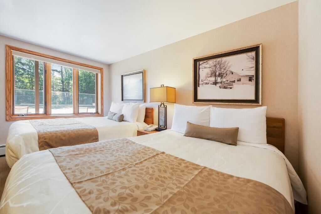 Une chambre d’hôtel avec deux lits, une grande fenêtre, un tableau encadré au mur et une table de chevet avec une lampe.