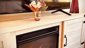 A modern living room with a fireplace, wooden cabinetry, and a vase with flowers on the mantel. - Modern LoSo Retreat|Walk to Breweries & Light Rail (Charlotte)