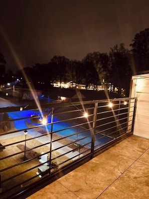 A pool area with a glass railing, a small building, and trees in the background.