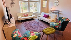 A living room with a sofa, two armchairs, a coffee table, a rug, and a clock on the wall. - Modern LoSo Retreat|Walk to Breweries & Light Rail (Charlotte)