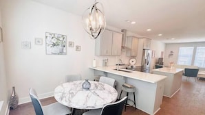 A modern kitchen with a marble island, black chairs, and a hanging light fixture. - Modern LoSo Retreat|Walk to Breweries & Light Rail (Charlotte)