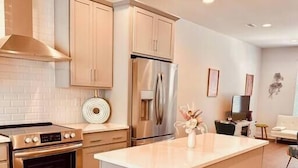 A modern kitchen with stainless steel appliances, a central island, and light-colored cabinetry. - Modern LoSo Retreat|Walk to Breweries & Light Rail (Charlotte)